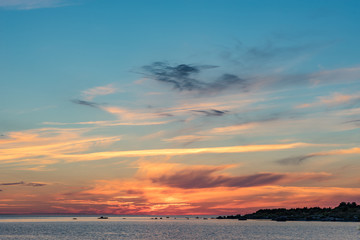 Evening sunlight on coast, pink clouds, blue sky reflection on water. Beach in summer. Seaside natural environment. Shore in Harilaid, small island in Estonia. Nature Reserve in North Europe