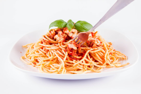 Spaghetti bolognese eaten with a fork decorated with basil on a white background