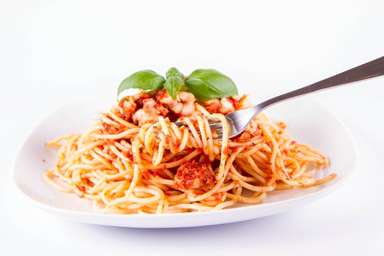 Spaghetti bolognese eaten with a fork decorated with basil on a white background