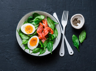 Delicious brunch - spinach, smoked salmon, soft boiled egg on a dark background, top view. Healthy eating diet concept