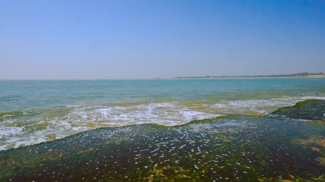 Waves crashing and sending up spray on the moss covered rocks of Nagaon beach Diu, Gujarat, India
