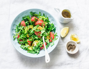 Avocado, grapefruit, rocket salad with mustard olive oil salad dressing on light background, top view. Vegetarian diet food concept