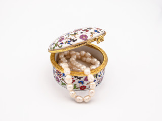 Beautifully ornamented porcelain jewelry box with a floral motive and a vintage flair with a sea pearls necklace showing from the inside isolated on a white background