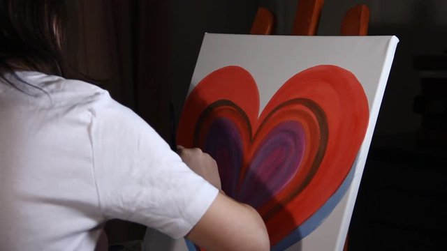 close up of woman artist painting a big red heart on the easel in the dark