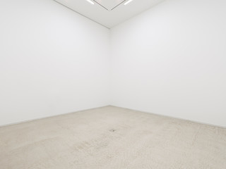 A view of a white painted interior of an empty room or an art gallery with a fluorescent lighting and concrete floors