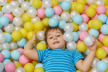Fototapeta na wymiar child of three years old is playing in a ball pool. boy smiling spends fun time in the nursery.