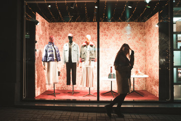 Portrait of a girl on the background of a fashion store showcase. Girl walks at the window of a...