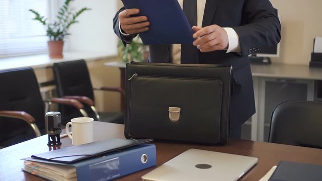 Experienced lawyer putting contract to suitcase in office going to court. White-collar taking document folder from workplace desk to carry in briefcase.
