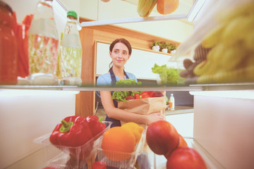 Portrait of female standing near open fridge full of healthy food, vegetables and fruits. Portrait of female