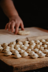 Fototapeta na wymiar Uncooked russian pelmeni on cutting board and ingredients for homemade pelmeni on white table. Process of making pelmeni, ravioli or dumplings with meat