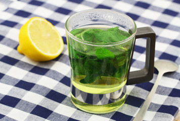 Fresh mint tea in transparent glass and half a lemon on checkered cloth
