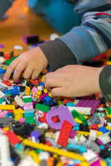 Close up of colorful plastic bricks on the floor. Early learning. Children's plastic constructor on the floor. Children's hands play a little constructor. vertical photo.