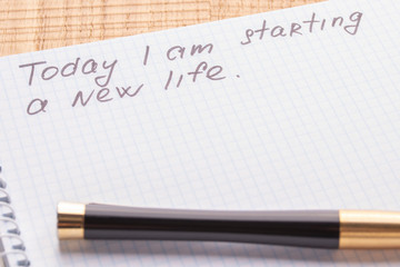 Top view workplace notebook and pen on wood table background. Inscription - Today I am starting a new life.