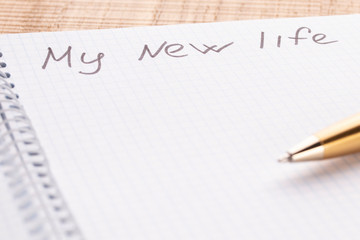 Top view workplace notebook and pen on wood table background, retro effect. The inscription is my new life.