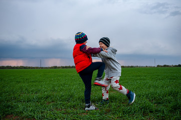 Two happy children playing in field sown with winter wheat against backdrop of rain clouds....