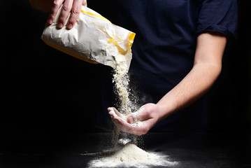 Hands of a cook in dark clothes are pouring flour