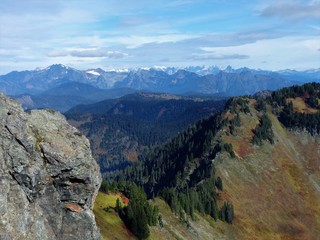 Fall colors cover the slope of a mountain with the rugged peaks of the North Cascades