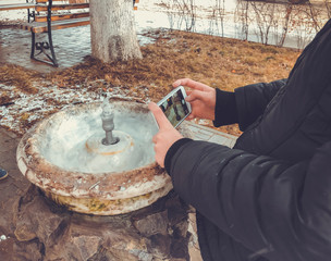 Child takes a photo. City fountain for drinking water flowing from the old column in city park. Flowing water for people 
