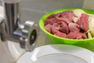 Pieces of the fresh meat lie in a bowl near the meat grinder in the kitchen