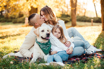 Fototapeta premium Happy beautiful family with dog labrador is having fun are sitting on green grass in park.