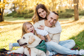 Fototapeta premium Happy beautiful family with dog labrador is having fun are sitting on green grass in park.