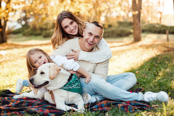 Fototapeta premium Happy beautiful family with dog labrador is having fun are sitting on green grass in park.