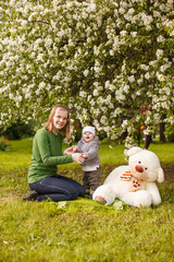 Fototapeta premium Baby with mother in the park in the rays of sunset. Toddler with mom on the nature outdoors. Backlight. Summertime family scene