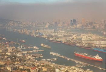 View from the air of ships docked at harbor against cityscape obscured by dense air pollution close...