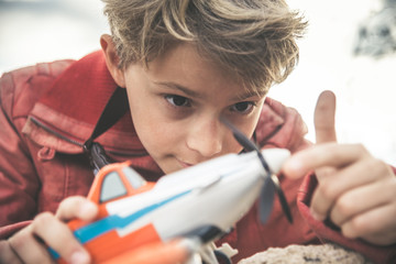 Close up of a little smiling boy playing with a small plane in a sunny day, dreaming about being an airplane pilot. Young and happy kid thinking about planes and pilots. Dreaming to be an aviator. © Fabio Principe