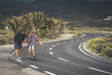 Fototapeta premium Dad teaches his son to use skateboard, father son spend time together learning to skate, blond striped knit boy with man who helps him skater spending quality day with family