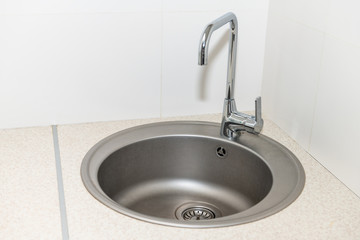 New modern faucet and kitchen room sink closeup with round stainless steel basin and countertop in model house home apartment in corner
