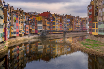 Colorful yellow, red, green houses alongside the Onyar river with reflection on the water in Girona Catalonia region Spain