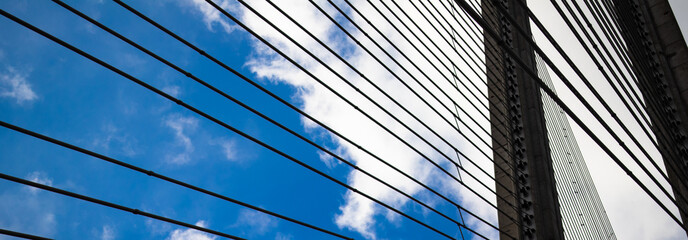 Obraz premium fragment of a bridge with a pylon and steel cables against a blue sky with white clouds