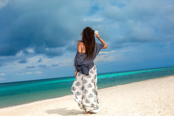 beautiful fashionable woman walking on the beach with frangipani flower