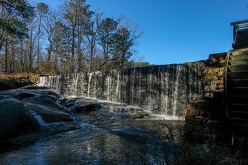 The morning sunshine strikes upon the dam and waterfall at Historic Yates Mill County Park in Raleigh North Carolina.
