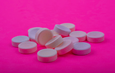Multi-color tablets (pills) on pink fuchsia color background.