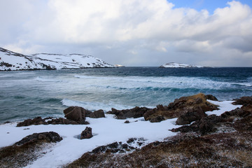 Russian Arctic View, North. Sky with clouds and blue sky reflection in water with waves and snow mountains background with stones grass foreground. Picturesque landscape view, nature scenery beauty