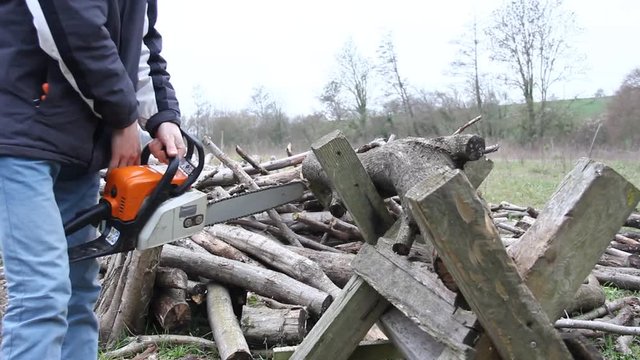 young man cutting wood for fire with a professional chainsaw