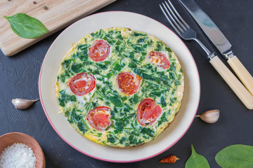 Spinach frittata ,italian omelet with cherry tomatoes in a plate on a dark background. Healthy food conception