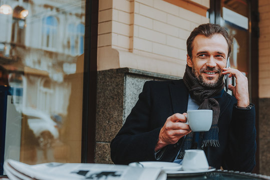 Joyful trendy man is communicating on smartphone in cafe