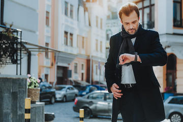 Stylish businessman in black coat is hurrying in city