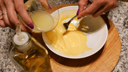 Female hands preparing homemade mayonnaise with egg yolk, lemon juice and olive oil