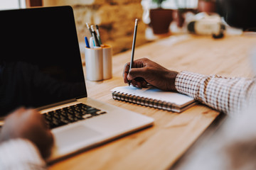 Close up of laptop and person making notes in notebook