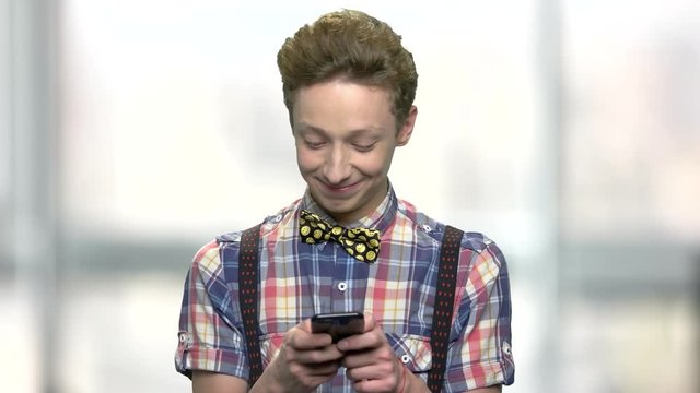 Smiling teen guy using his cell phone. Cute teenage boy texting a message on mobile phone. Abstract blurred background.