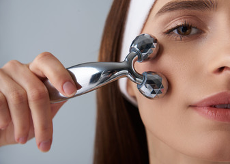 Charming girl with perfect skin using facial massager