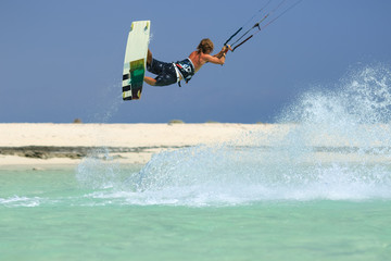 Professional kite boarding rider sportsman with kite in sky jumps high acrobatics kiteboarding trick with grab of kiteboard and huge water splash. Recreational activity, extreme active air sports