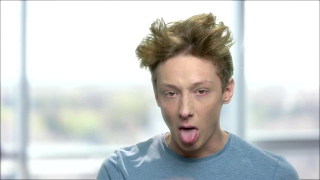 Rude teen boy making grimace. Funny teenage boy teasing someone and looking at camera against blurred background.
