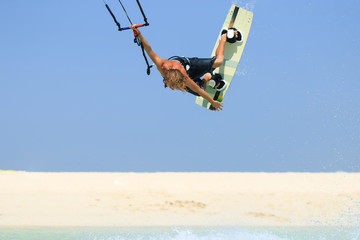 Professional kite boarding rider sportsman with kite in sky jumps high acrobatics kiteboarding trick with grab of kiteboard and huge water splash. Recreational activity, extreme active air sports