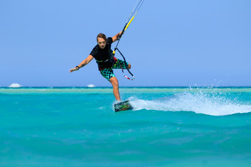 Kite surfing man surf sportsman with kite in sky on board in blue sea riding waves with water splash. Recreational activity, water sports, action, hobby and fun in summer time. Kiteboarding sport
