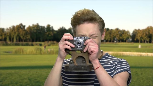 Teenage boy using vintage camera outdoor. Cute teen guy taking picture with retro photo camera on nature background. Beautiful sunny day.